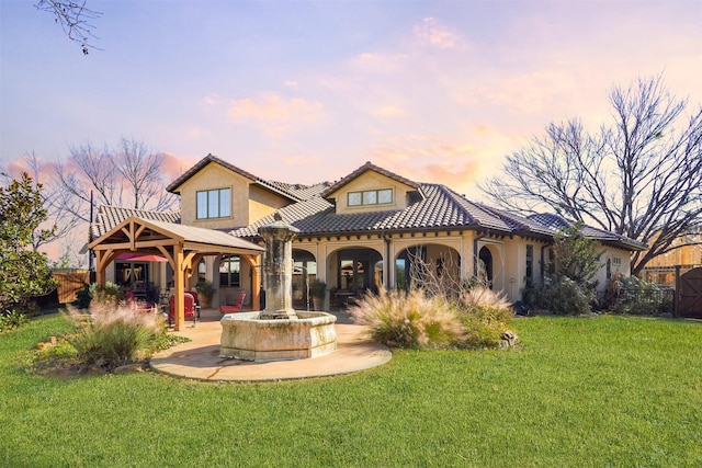 back house at dusk featuring a yard, a gazebo, and a patio