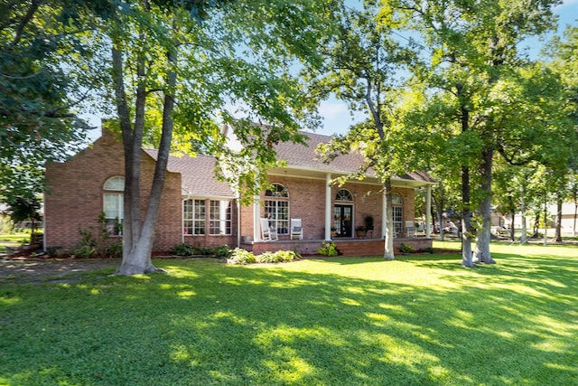 view of front facade featuring brick siding, a porch, a shingled roof, and a front lawn