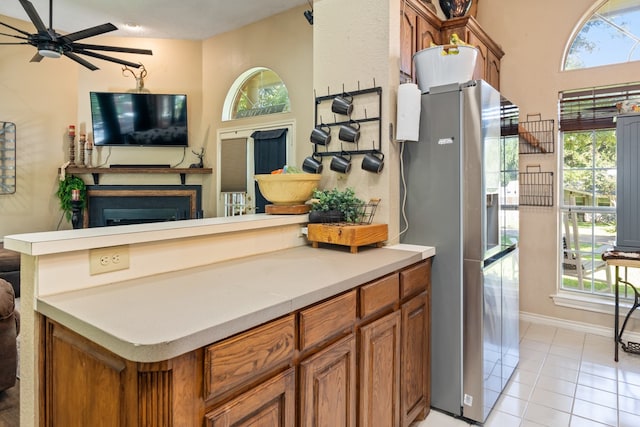 kitchen featuring stainless steel refrigerator with ice dispenser, ceiling fan, a fireplace, and light tile patterned floors