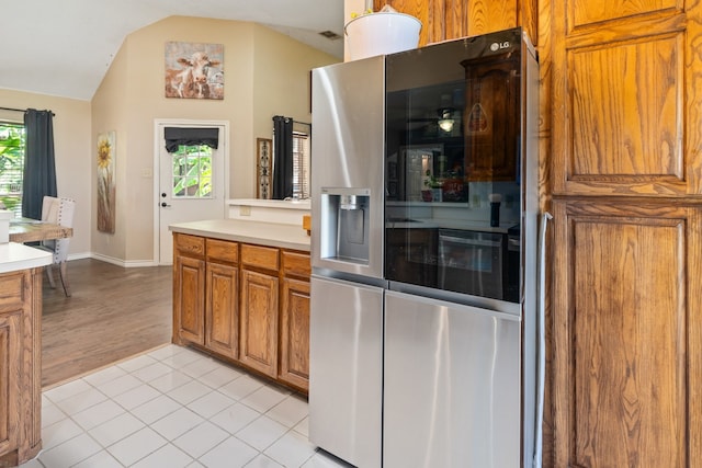 kitchen featuring brown cabinets, stainless steel fridge, light tile patterned flooring, light countertops, and vaulted ceiling