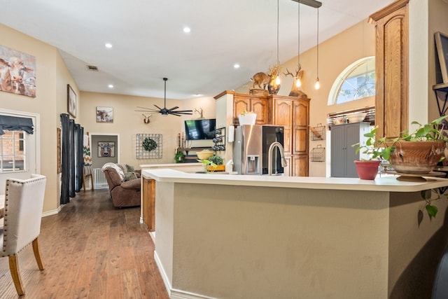 kitchen featuring wood finished floors, a peninsula, light countertops, stainless steel refrigerator with ice dispenser, and pendant lighting