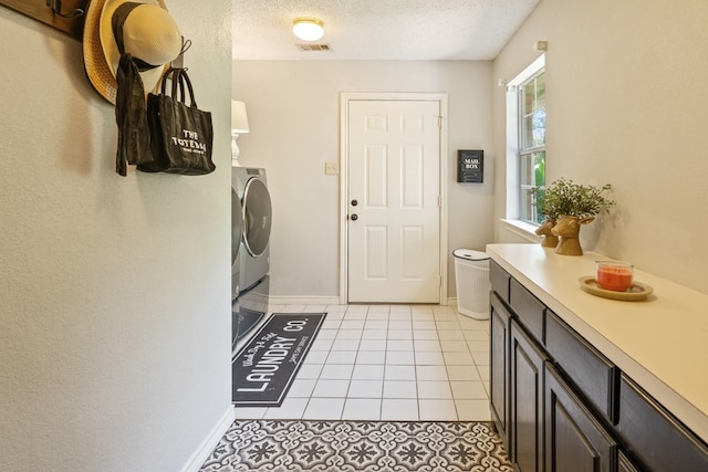 laundry area featuring cabinets, light tile patterned flooring, washing machine and clothes dryer, and a textured ceiling