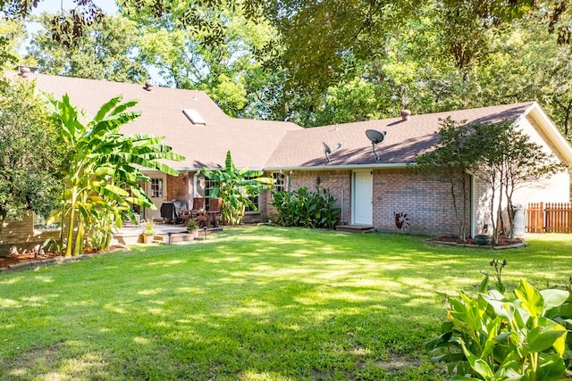 view of front of house featuring a patio, fence, roof with shingles, a yard, and brick siding