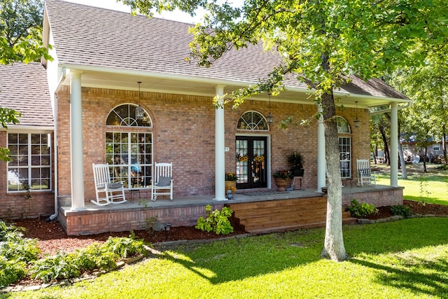 exterior space with brick siding, a shingled roof, a porch, a lawn, and french doors