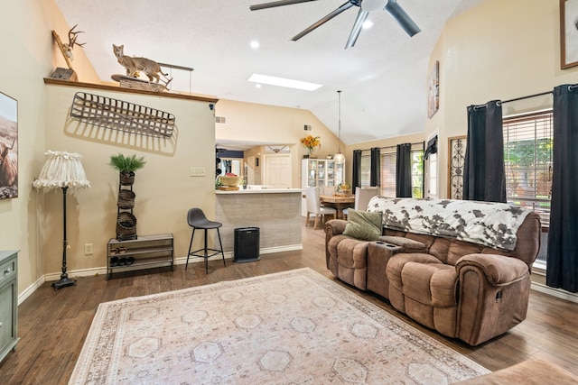 living room featuring dark wood-type flooring, vaulted ceiling with skylight, a textured ceiling, and ceiling fan