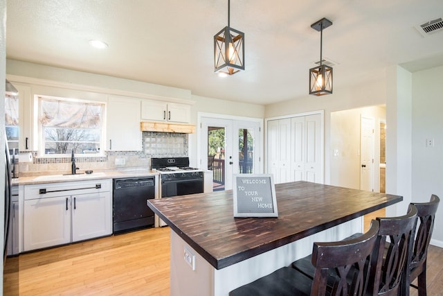 kitchen with butcher block countertops, hanging light fixtures, black dishwasher, range with gas stovetop, and white cabinets