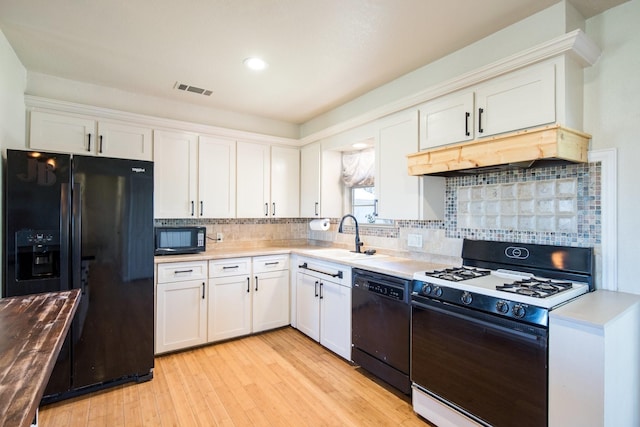 kitchen with sink, white cabinets, decorative backsplash, black appliances, and light wood-type flooring