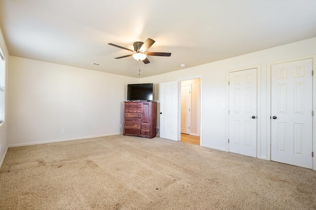 unfurnished bedroom featuring ceiling fan, light carpet, and two closets