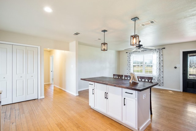 kitchen with wood counters, white cabinetry, a center island, light hardwood / wood-style flooring, and pendant lighting