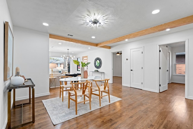 dining area featuring beamed ceiling, wood-type flooring, ceiling fan with notable chandelier, and a textured ceiling