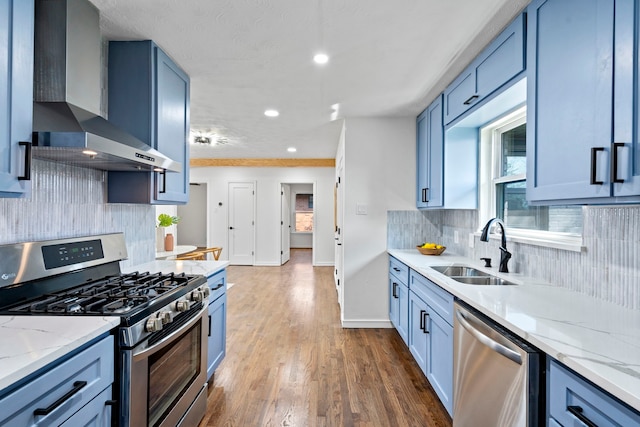 kitchen with wall chimney range hood, light stone countertops, sink, and appliances with stainless steel finishes