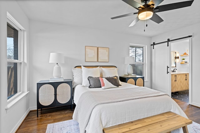 bedroom with sink, dark wood-type flooring, ceiling fan, connected bathroom, and a barn door