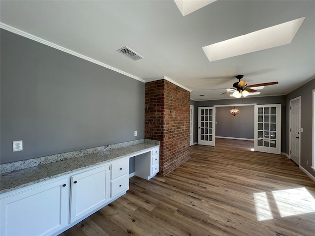 interior space with crown molding, white cabinetry, a skylight, light stone counters, and built in desk