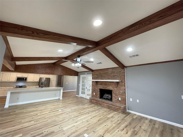 unfurnished living room featuring vaulted ceiling with beams, ceiling fan, a brick fireplace, light wood-type flooring, and french doors