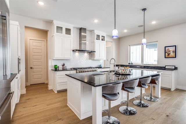 kitchen with sink, light hardwood / wood-style flooring, an island with sink, and wall chimney exhaust hood