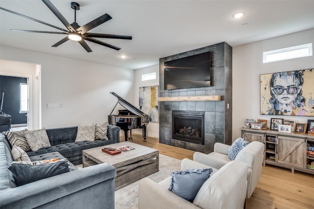 living room with a wealth of natural light, a tile fireplace, ceiling fan, and light wood-type flooring