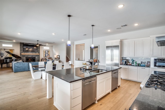 kitchen with pendant lighting, sink, appliances with stainless steel finishes, white cabinetry, and an island with sink