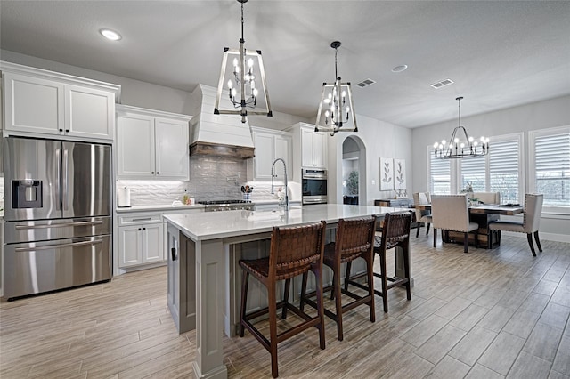 kitchen featuring stainless steel refrigerator with ice dispenser, sink, hanging light fixtures, a kitchen island with sink, and white cabinets