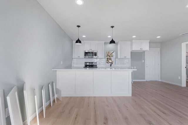 kitchen featuring decorative light fixtures, light hardwood / wood-style flooring, appliances with stainless steel finishes, white cabinets, and backsplash