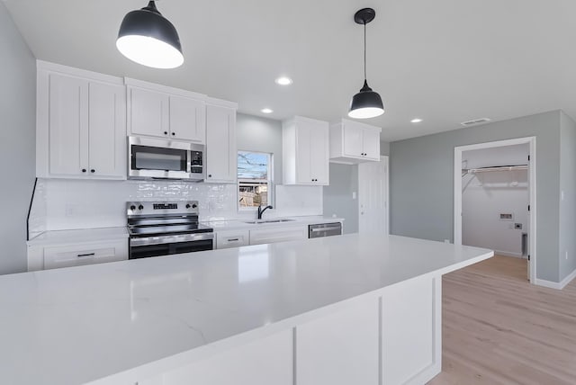 kitchen featuring hanging light fixtures, stainless steel appliances, sink, and white cabinets