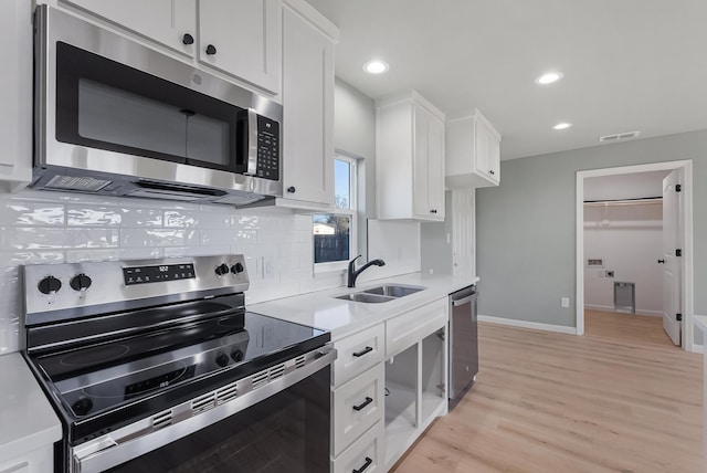 kitchen with sink, white cabinetry, stainless steel appliances, light hardwood / wood-style floors, and decorative backsplash