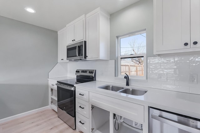 kitchen with sink, white cabinetry, stainless steel appliances, light hardwood / wood-style floors, and decorative backsplash