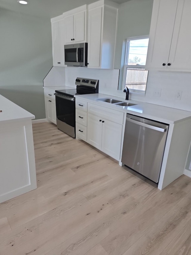 kitchen with stainless steel appliances, sink, white cabinets, and light hardwood / wood-style floors