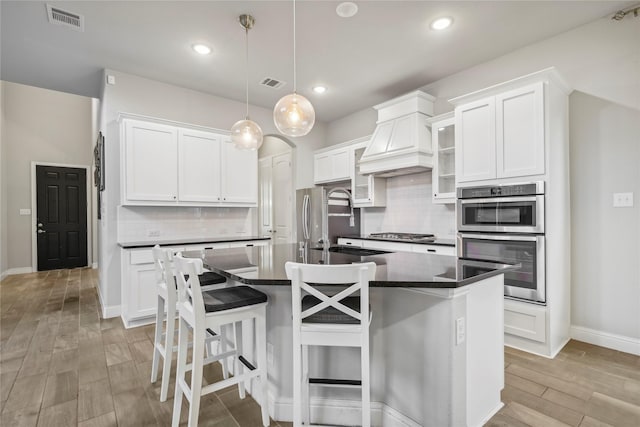 kitchen featuring hanging light fixtures, appliances with stainless steel finishes, a kitchen island with sink, and white cabinets