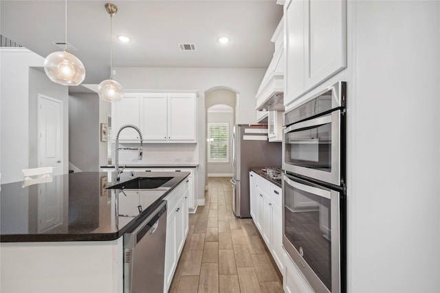 kitchen featuring sink, a center island with sink, hanging light fixtures, stainless steel appliances, and white cabinets