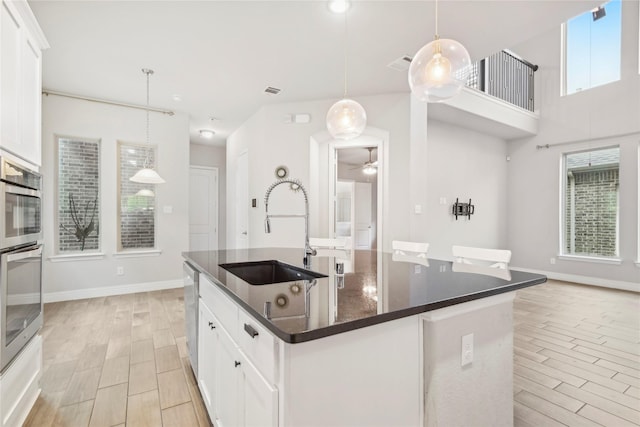 kitchen with a kitchen island with sink, sink, pendant lighting, and white cabinets