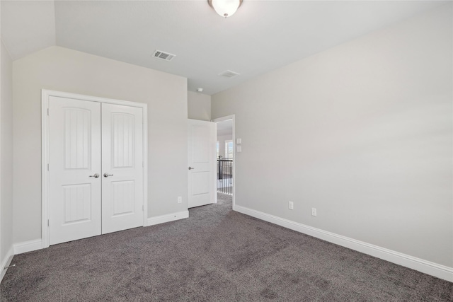 unfurnished bedroom featuring lofted ceiling, a closet, and dark colored carpet