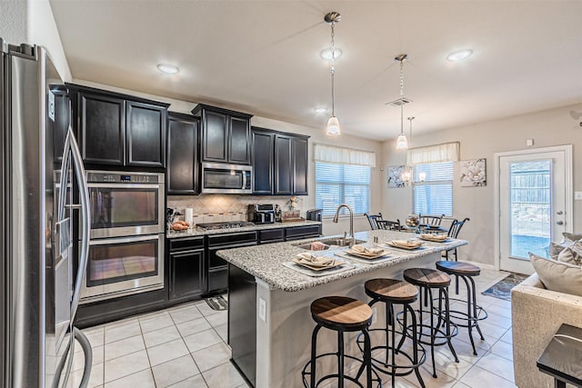 kitchen featuring sink, appliances with stainless steel finishes, hanging light fixtures, an island with sink, and decorative backsplash