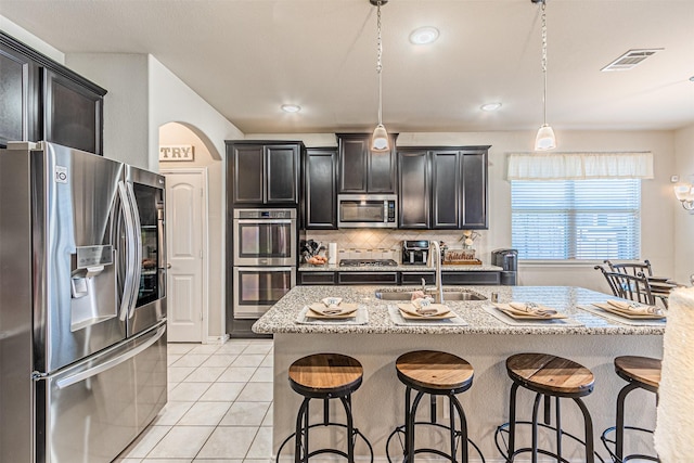 kitchen featuring sink, tasteful backsplash, hanging light fixtures, a center island with sink, and stainless steel appliances