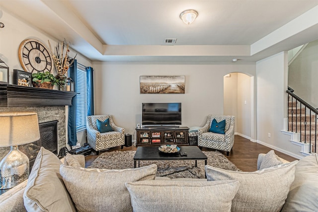 living room featuring a stone fireplace, hardwood / wood-style floors, and a tray ceiling