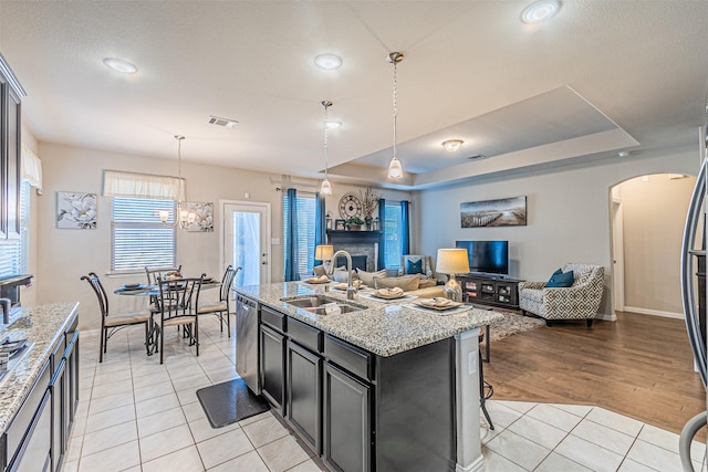 kitchen with an island with sink, sink, hanging light fixtures, light tile patterned floors, and light stone counters