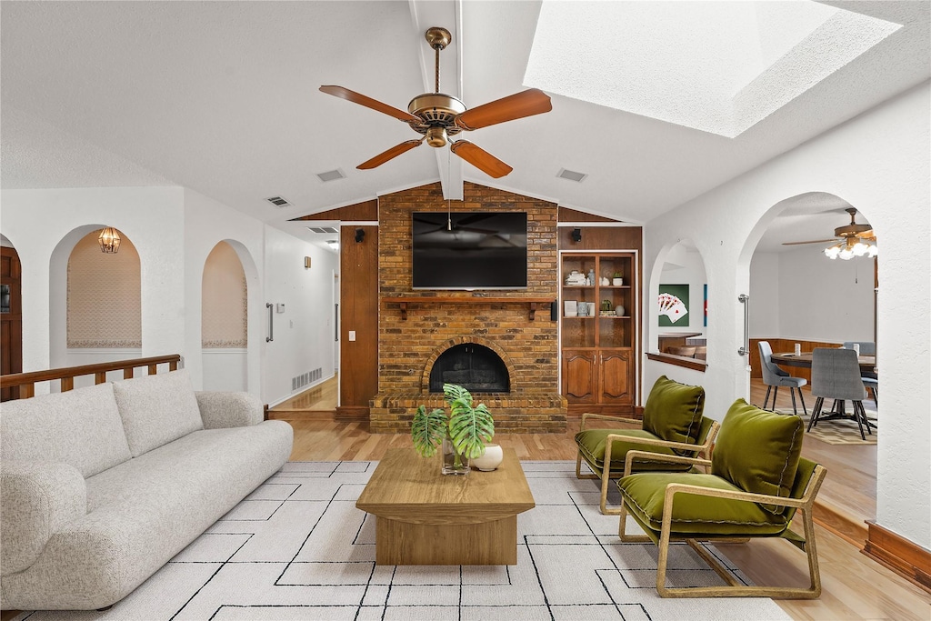 living room featuring vaulted ceiling, built in features, ceiling fan, light hardwood / wood-style floors, and a brick fireplace