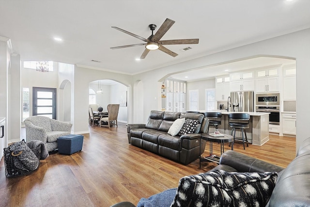 living room featuring light wood finished floors, visible vents, arched walkways, baseboards, and ornamental molding