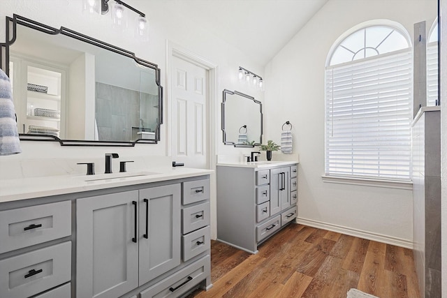 bathroom with wood finished floors, a sink, vaulted ceiling, a shower stall, and two vanities