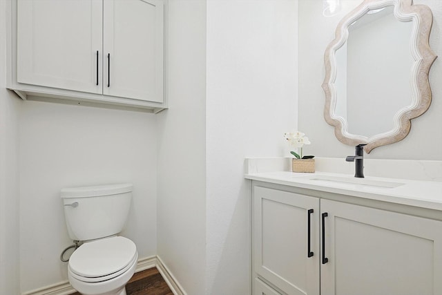 bathroom with toilet, wood finished floors, vanity, and baseboards