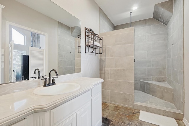 bathroom featuring stone tile floors, a walk in shower, and vanity