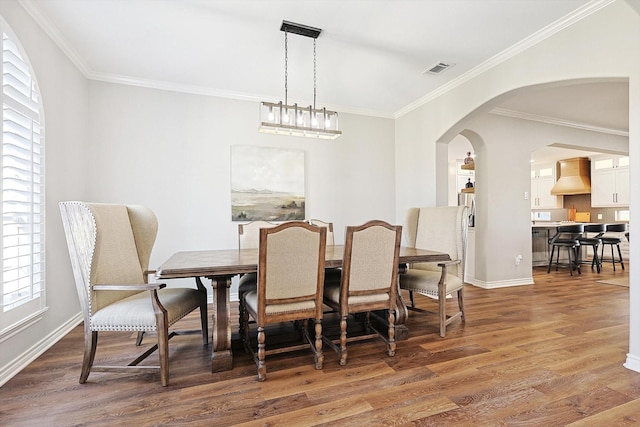 dining area with arched walkways, baseboards, wood finished floors, and crown molding