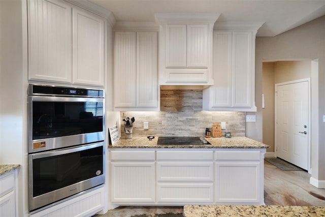 kitchen with black electric cooktop, double oven, light stone counters, and white cabinets