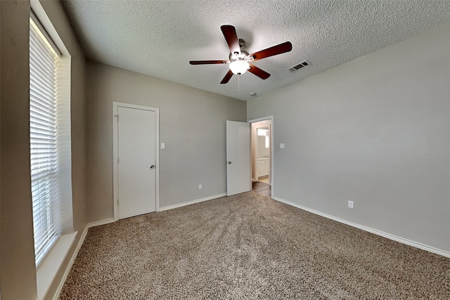 unfurnished bedroom with multiple windows, light colored carpet, a textured ceiling, and ceiling fan