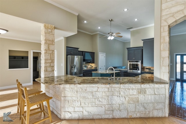 kitchen with appliances with stainless steel finishes, kitchen peninsula, sink, and light stone countertops