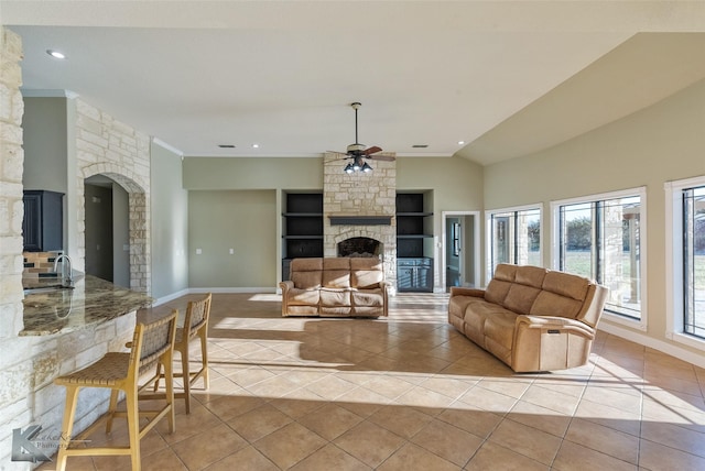 living room featuring lofted ceiling, ceiling fan, built in shelves, light tile patterned flooring, and a stone fireplace