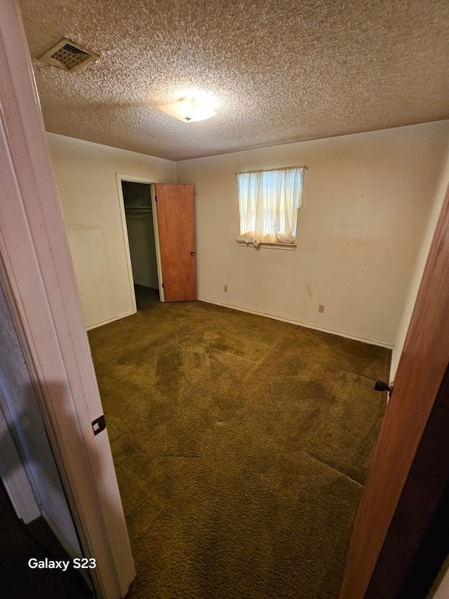 spare room featuring a textured ceiling and dark colored carpet