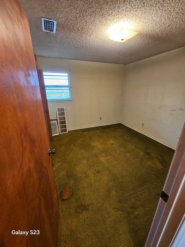 empty room with dark carpet and a textured ceiling