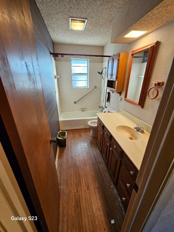 full bathroom with tiled shower / bath combo, vanity, hardwood / wood-style flooring, toilet, and a textured ceiling