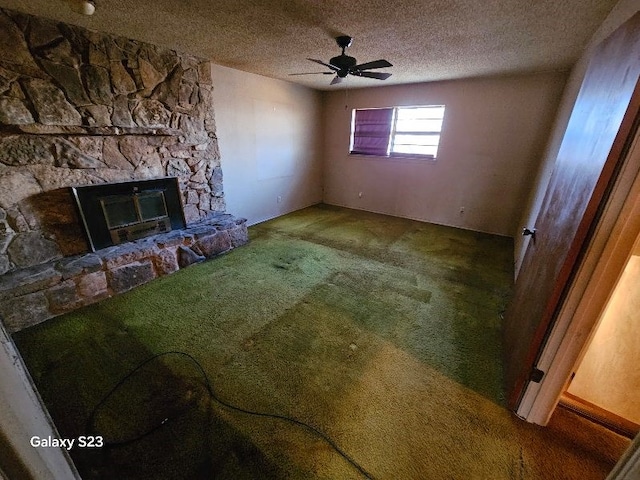 unfurnished living room with ceiling fan, a stone fireplace, carpet floors, and a textured ceiling