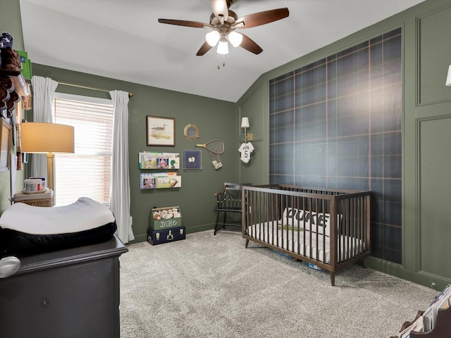 carpeted bedroom featuring a crib, lofted ceiling, and ceiling fan